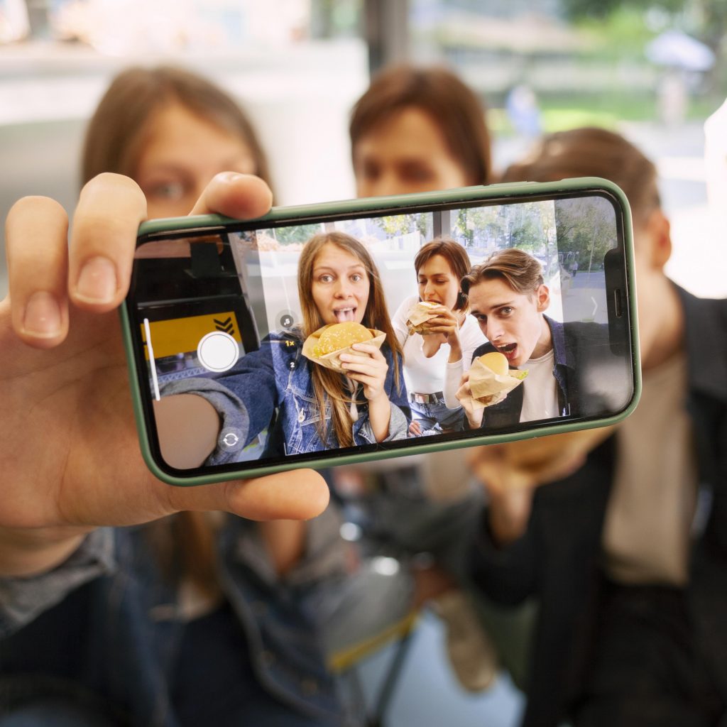 Groupe d’amis prenant un selfie en mangeant des burgers, capturant un moment de vie authentique – exemple de contenu vlog monté avec sincérité dans le cadre des services de montage vidéo à Lorient proposés par Keltic Prod